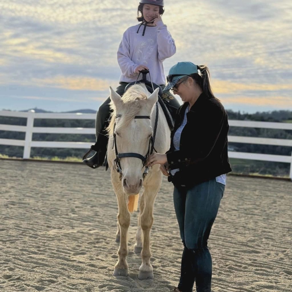 Jalaina smiling as a student connects with a horse in the arena